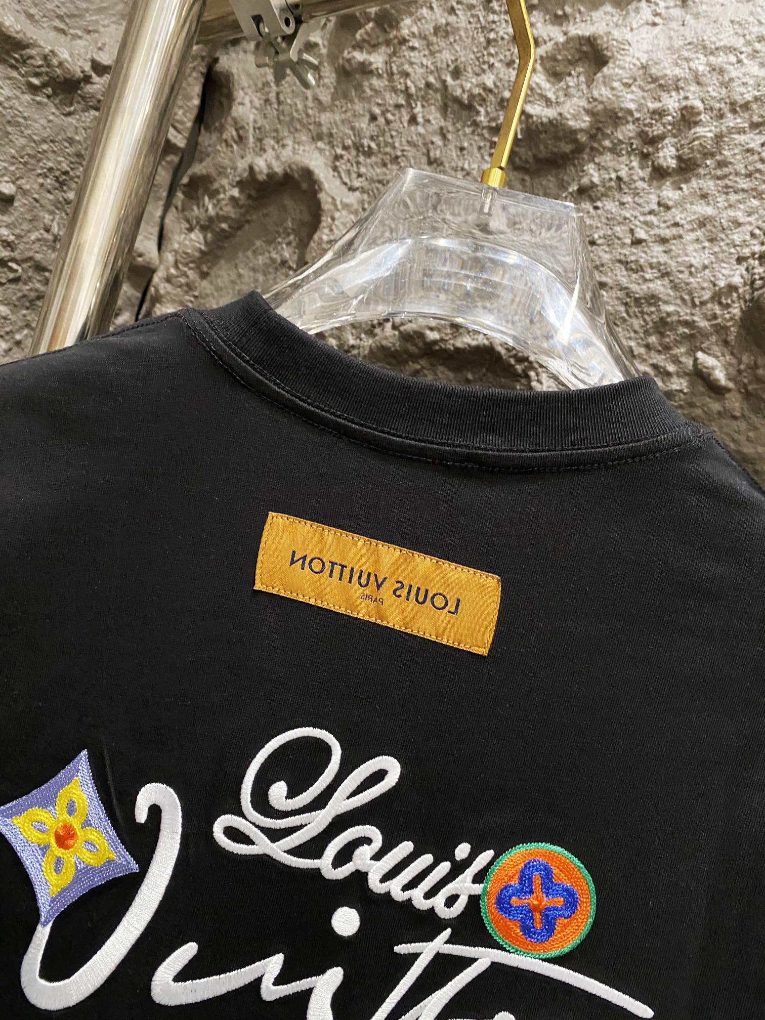 Black T-shirt front with colorful logo embroidery and yellow neck tag