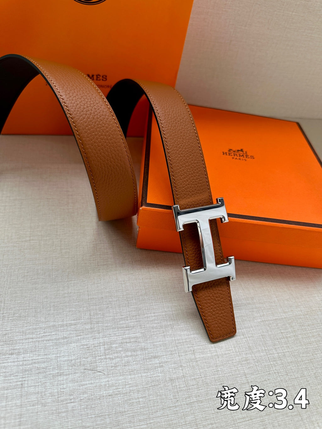 Leather belt with brown strap and silver-tone H buckle close-up, resting on box.