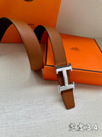 Leather belt with brown strap and silver-tone H buckle close-up, resting on box.