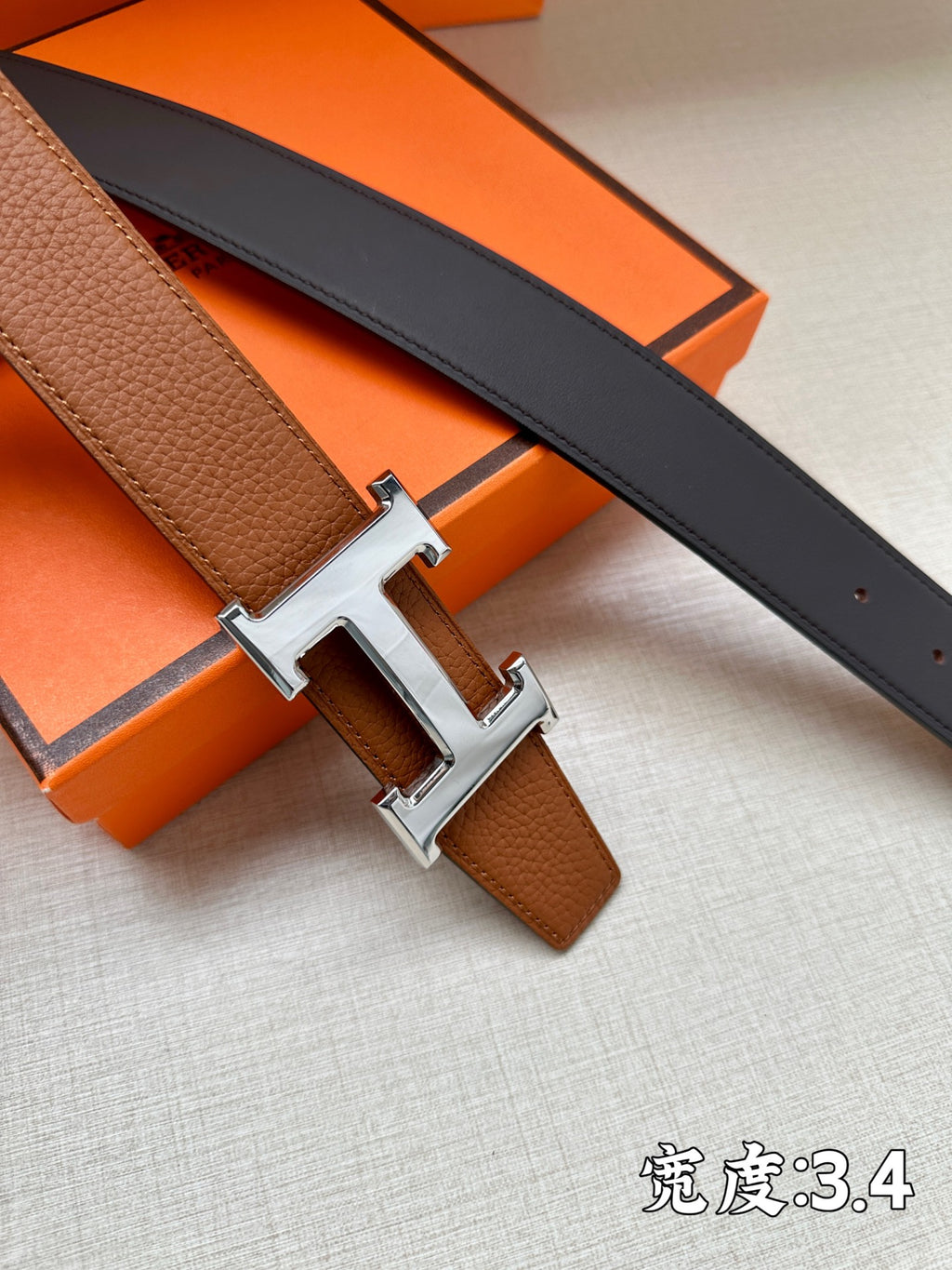 Leather belts with brown and dark straps, silver-tone H buckle centered on orange box.