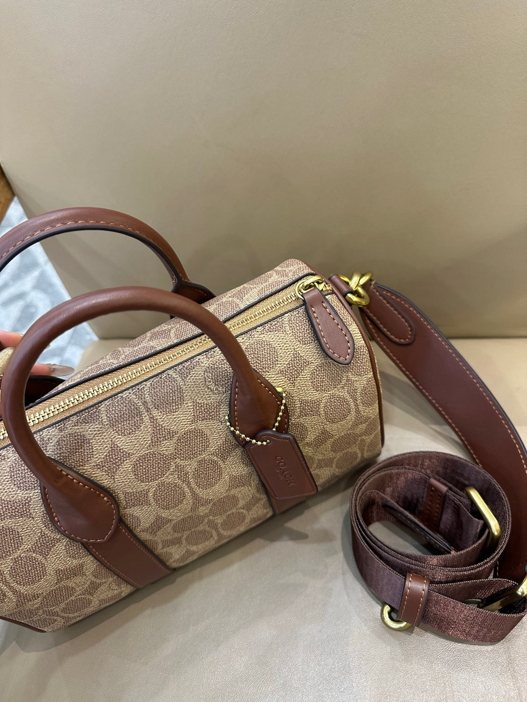 Coah small top-handle bag showing zipper pocket, tan logo canvas, brown leather trim, and chain pulls