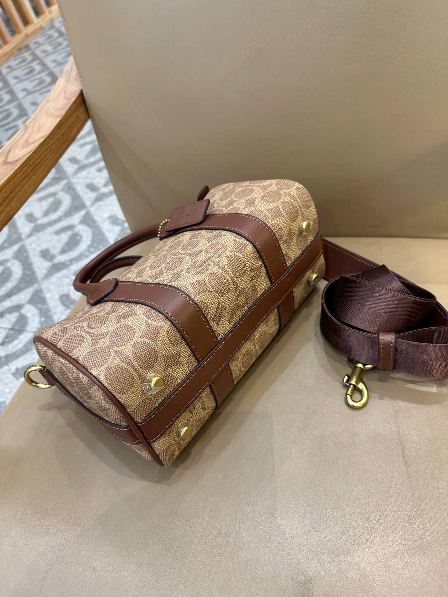 Coah mini bag with tan logo canvas, brown leather edges, top zipper, and crossbody strap