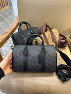 Coah bag with dark patterned exterior, top handles, and detachable crossbody strap