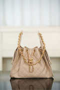 Quilted light beige shoulder bag with chain handles and CC emblem at center front.