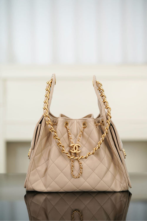Quilted light beige shoulder bag with chain handles and CC emblem at center front.
