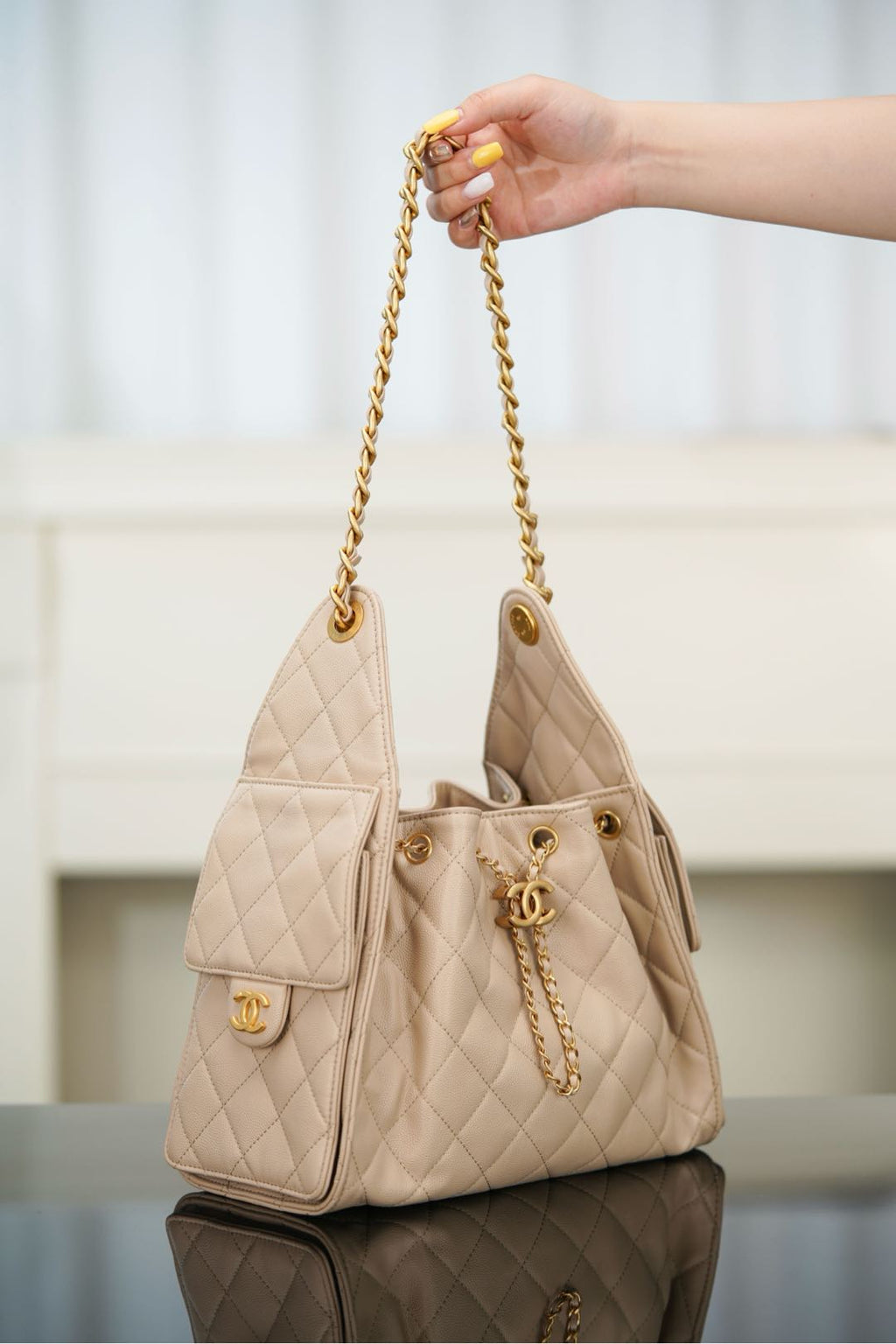 Quilted light beige shoulder bag held by chain strap, with small flap pocket front.