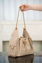 Quilted light beige shoulder bag held by chain strap, with small flap pocket front.