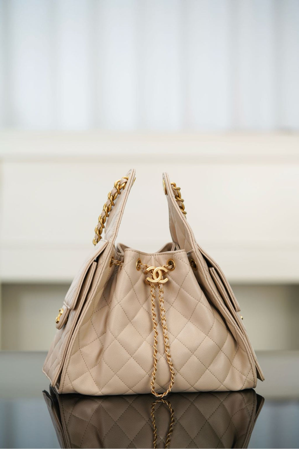 Quilted light beige shoulder bag with chain shoulder strap and front top pull.