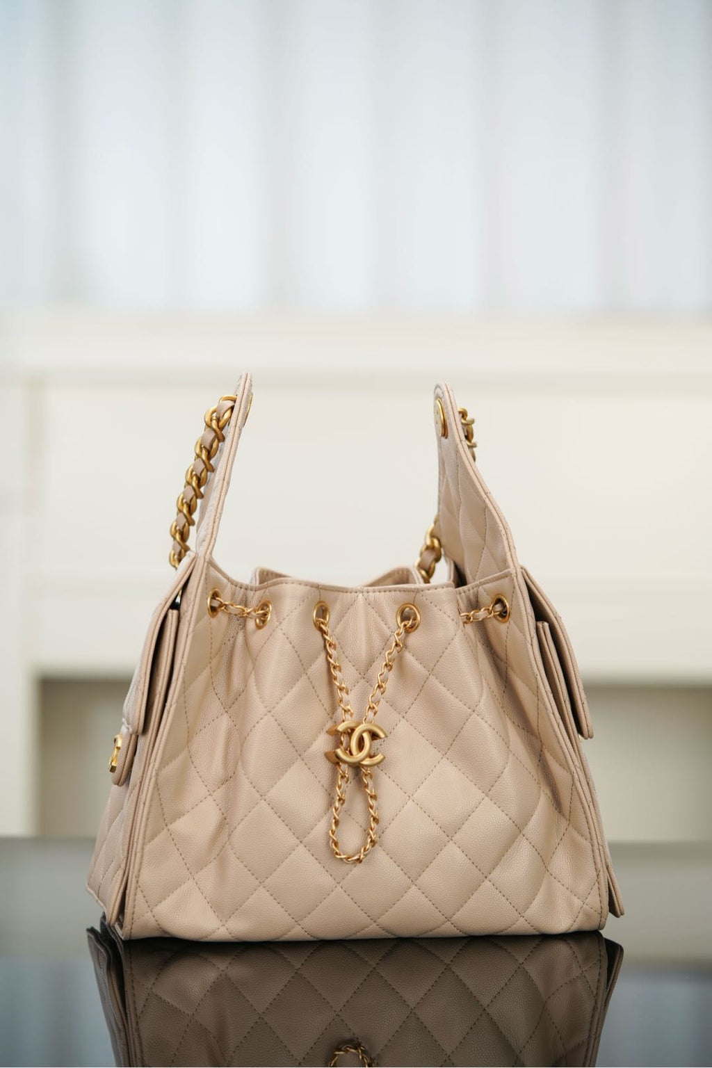 Quilted light beige shoulder bag with chain strap and CC emblem at center front.