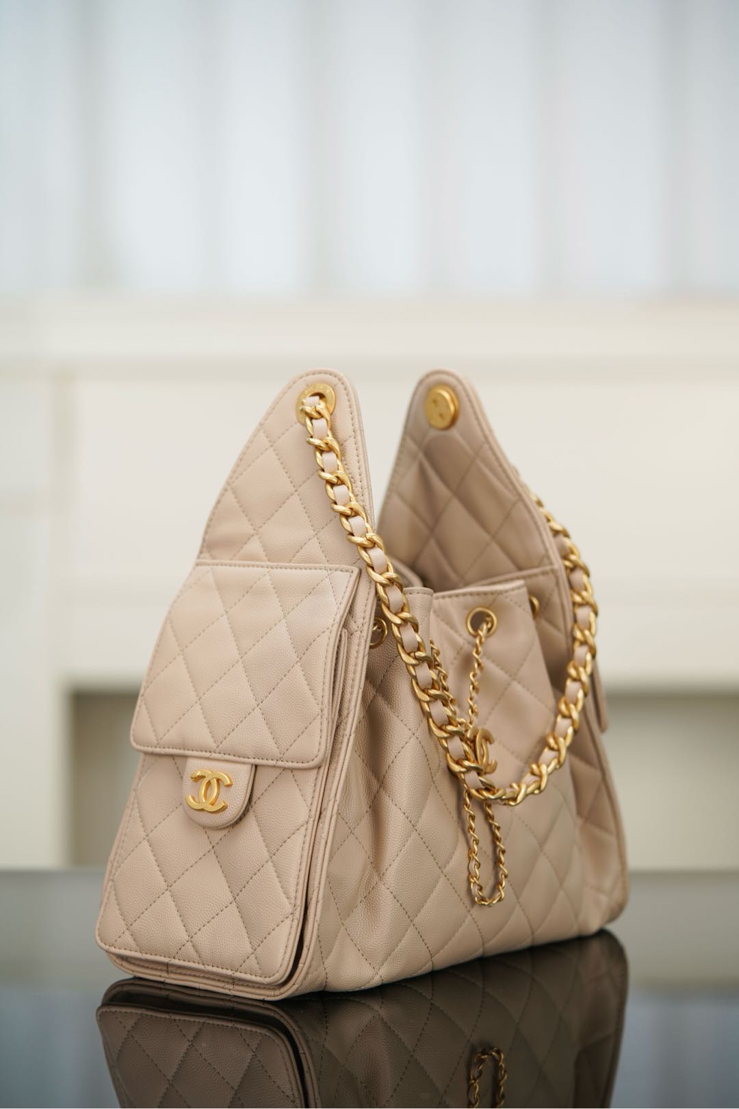 Quilted light beige shoulder bag side view with small flap pocket and chain strap.