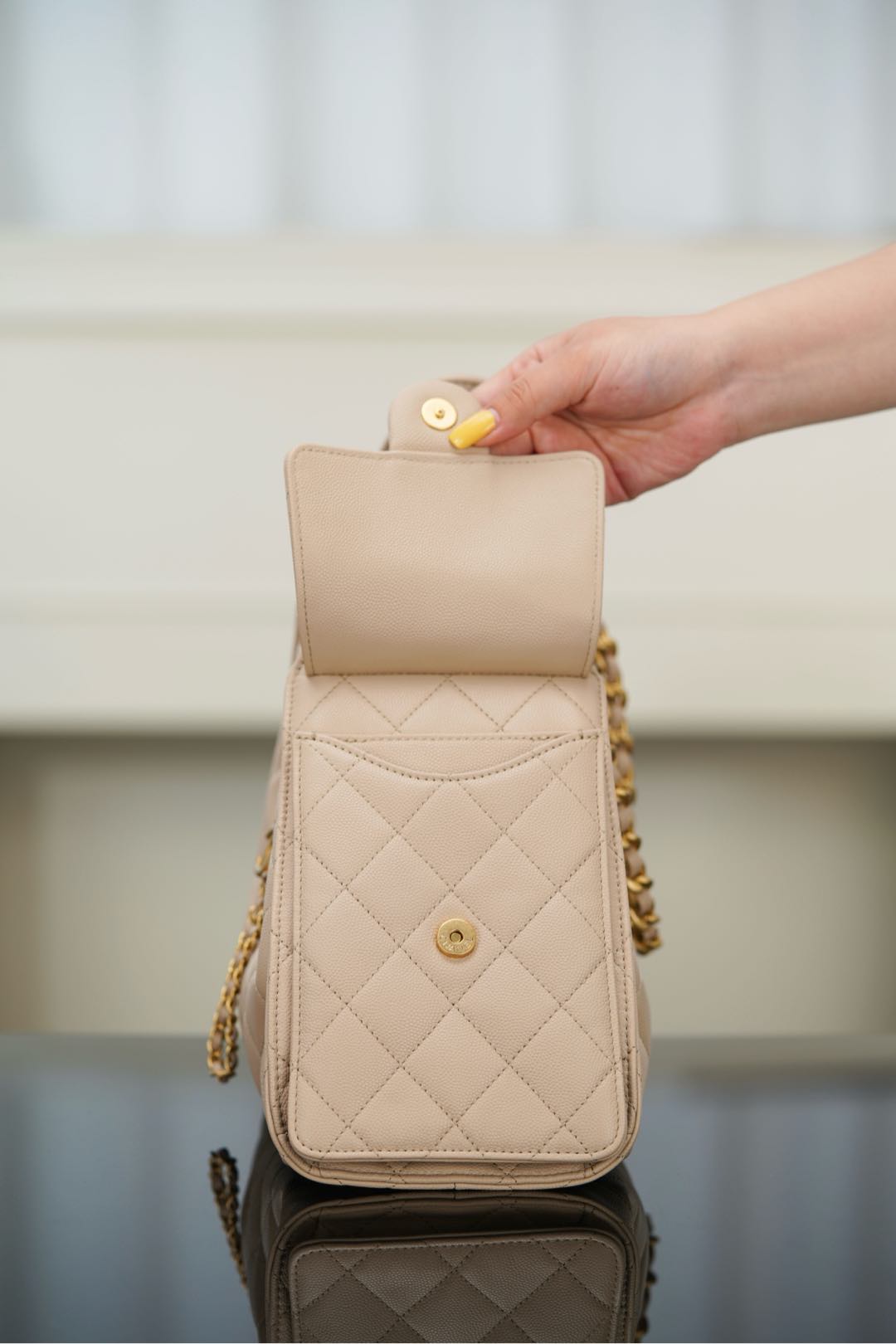 Quilted light beige bag with flap closure and small top button, chain strap attached.