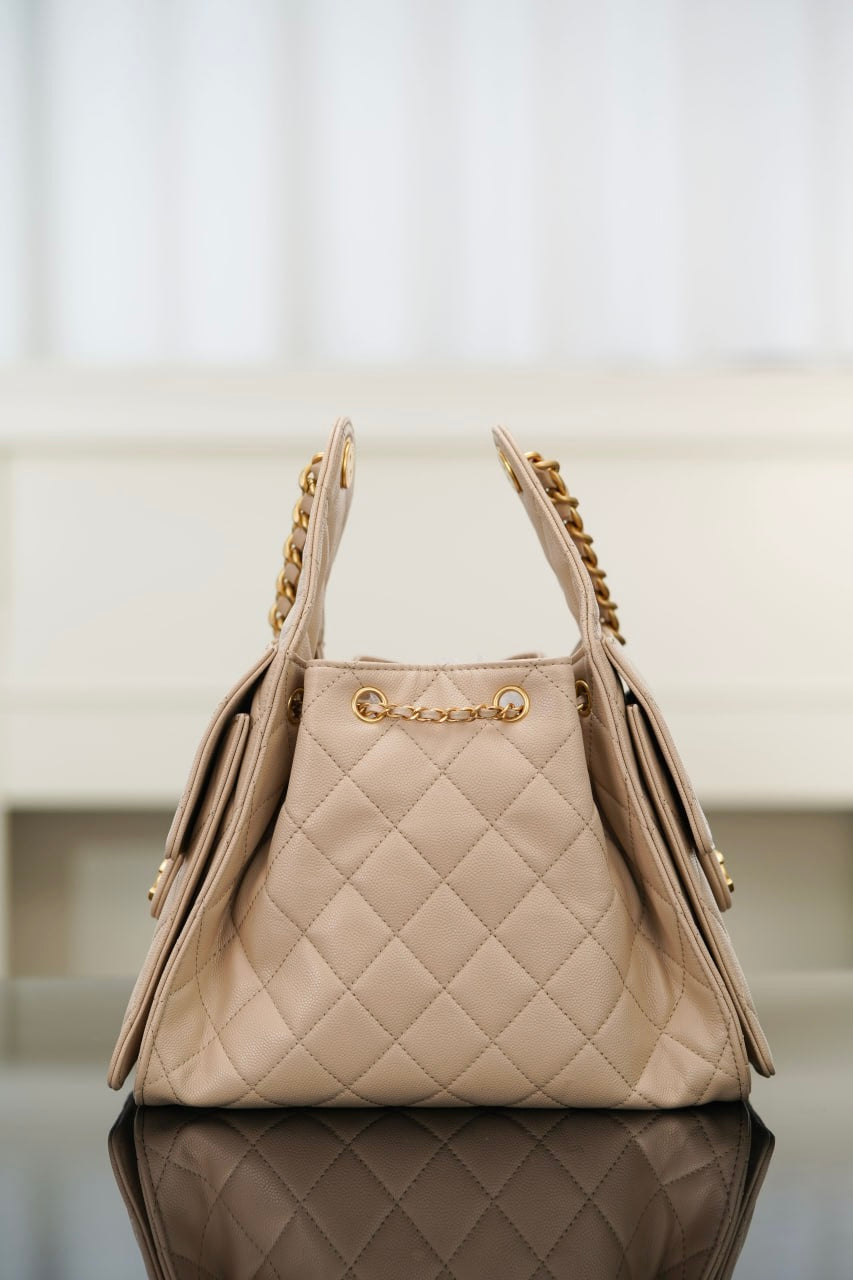 Quilted light beige shoulder bag with top handles and gold chain trim, side view.