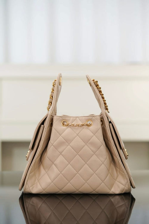Quilted light beige shoulder bag with top handles and gold chain trim, side view.