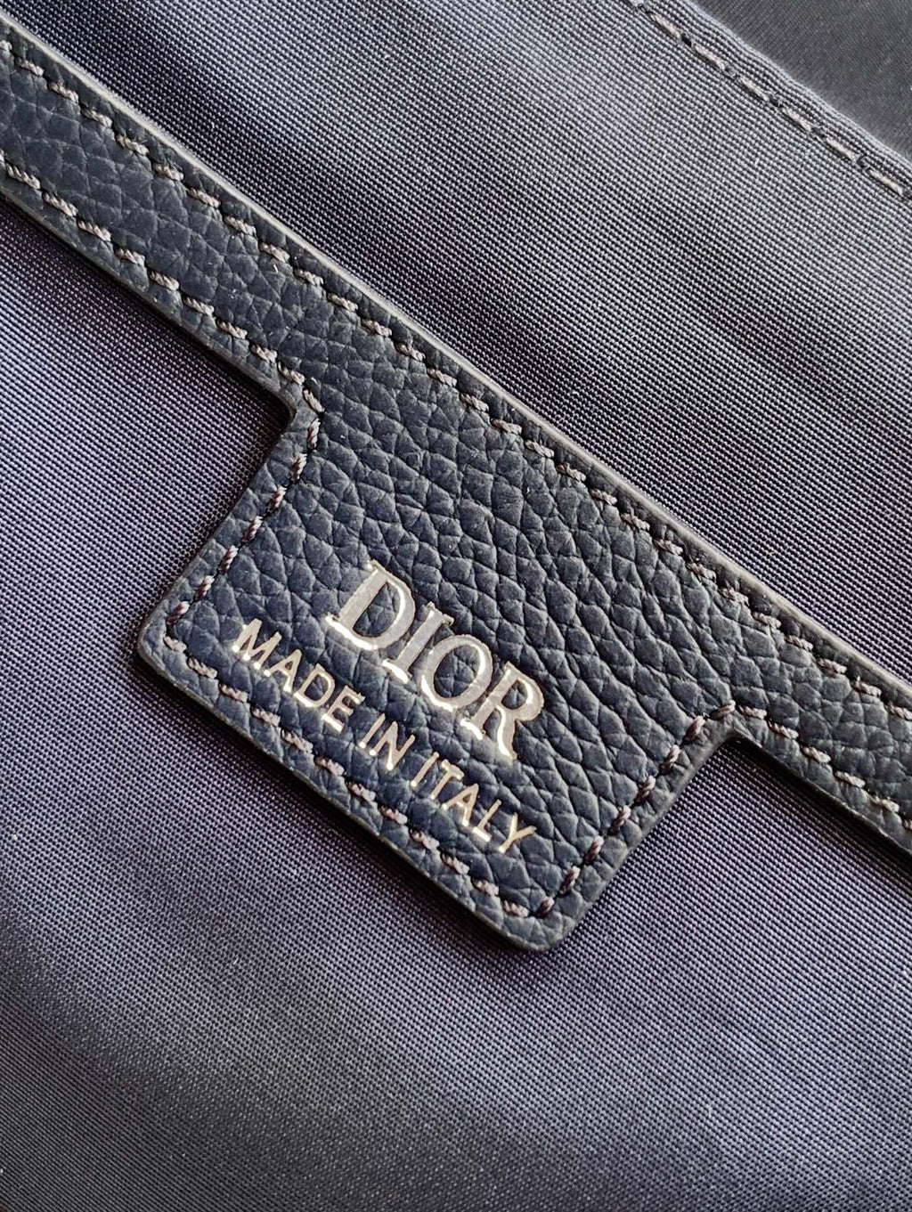 Dior blue leather bag close-up showing “DIOR” logo and “MADE IN ITALY” label