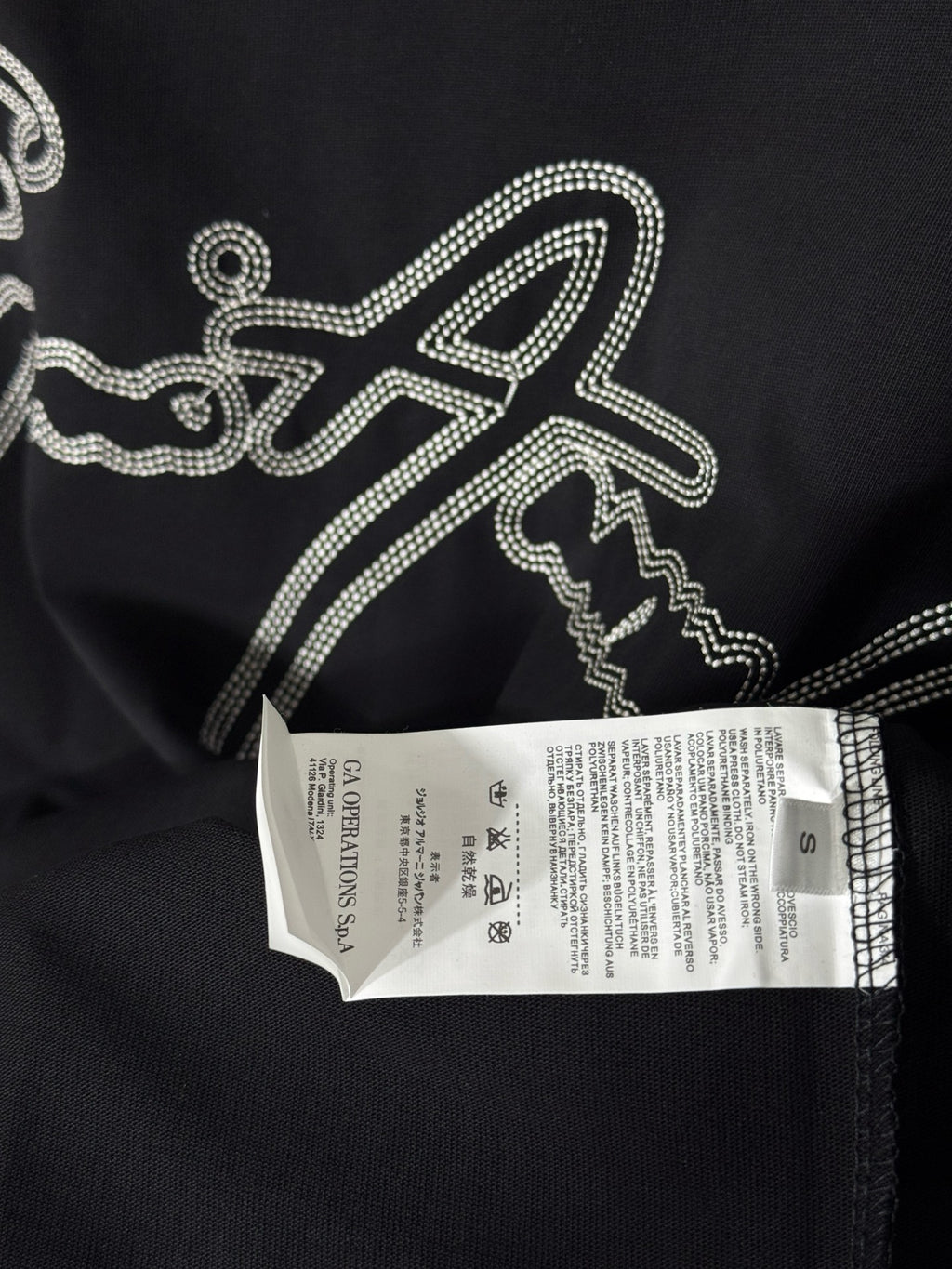 Black T-shirt with rhinestone script logo and white size label attached.