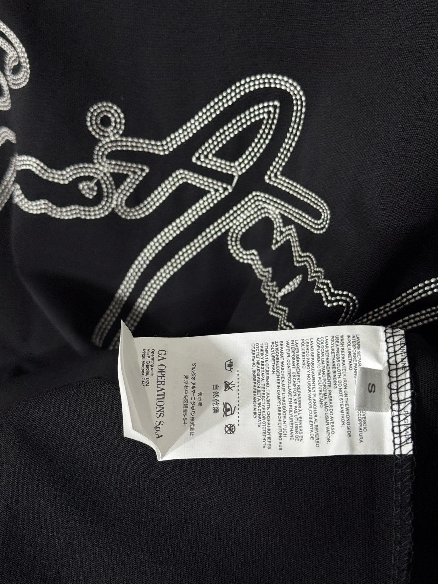Black T-shirt with rhinestone script logo and white size label attached.