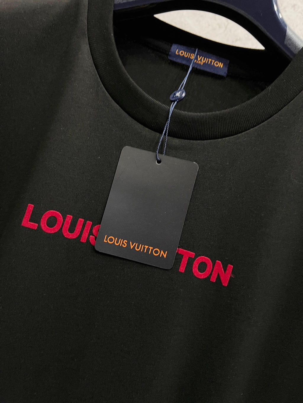 Black short-sleeve T-shirt with red Louis Vuitton text logo and hanging tag