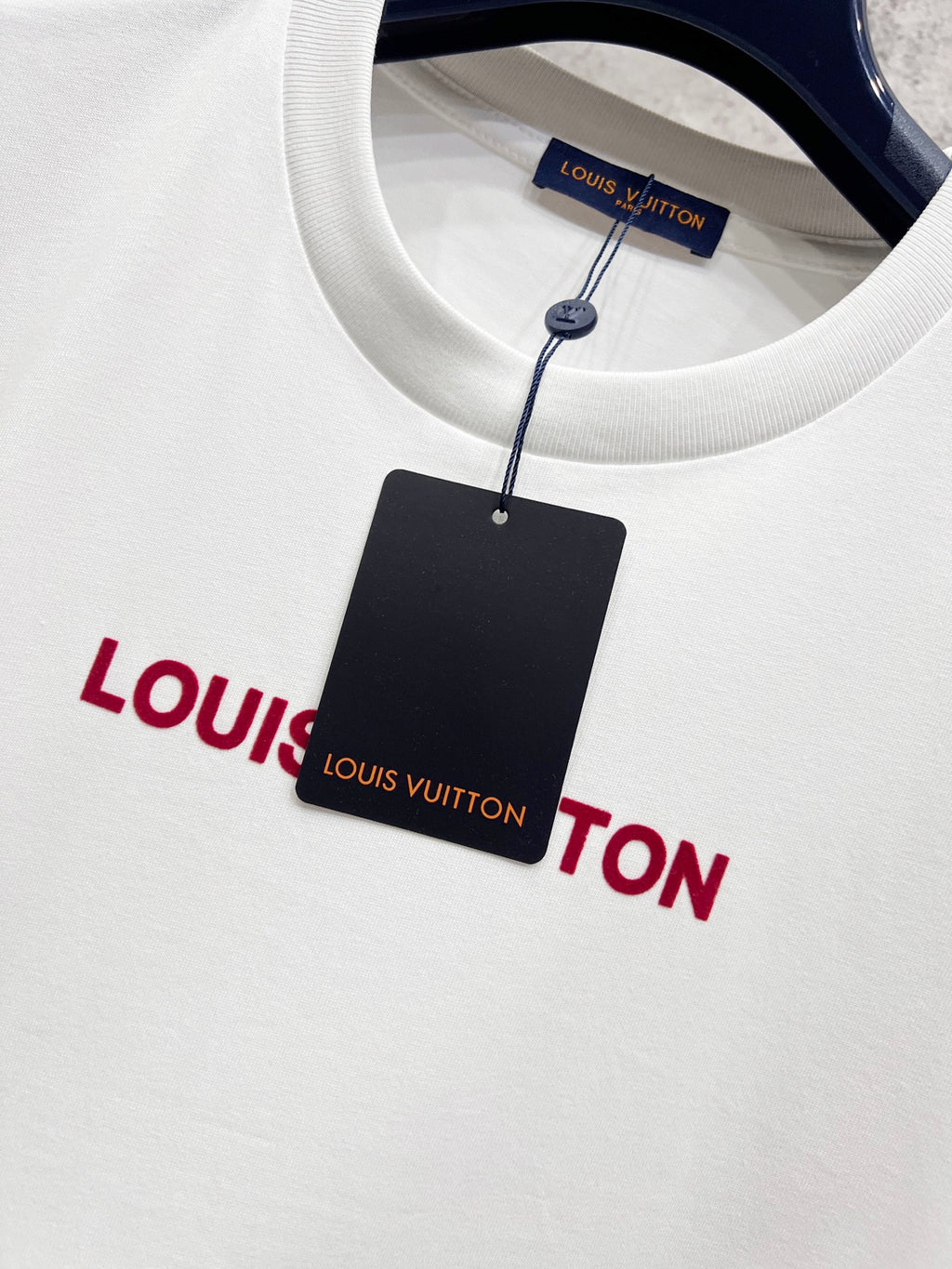 White T-shirt with red Louis Vuitton logo, plus black hang tag attached by string.