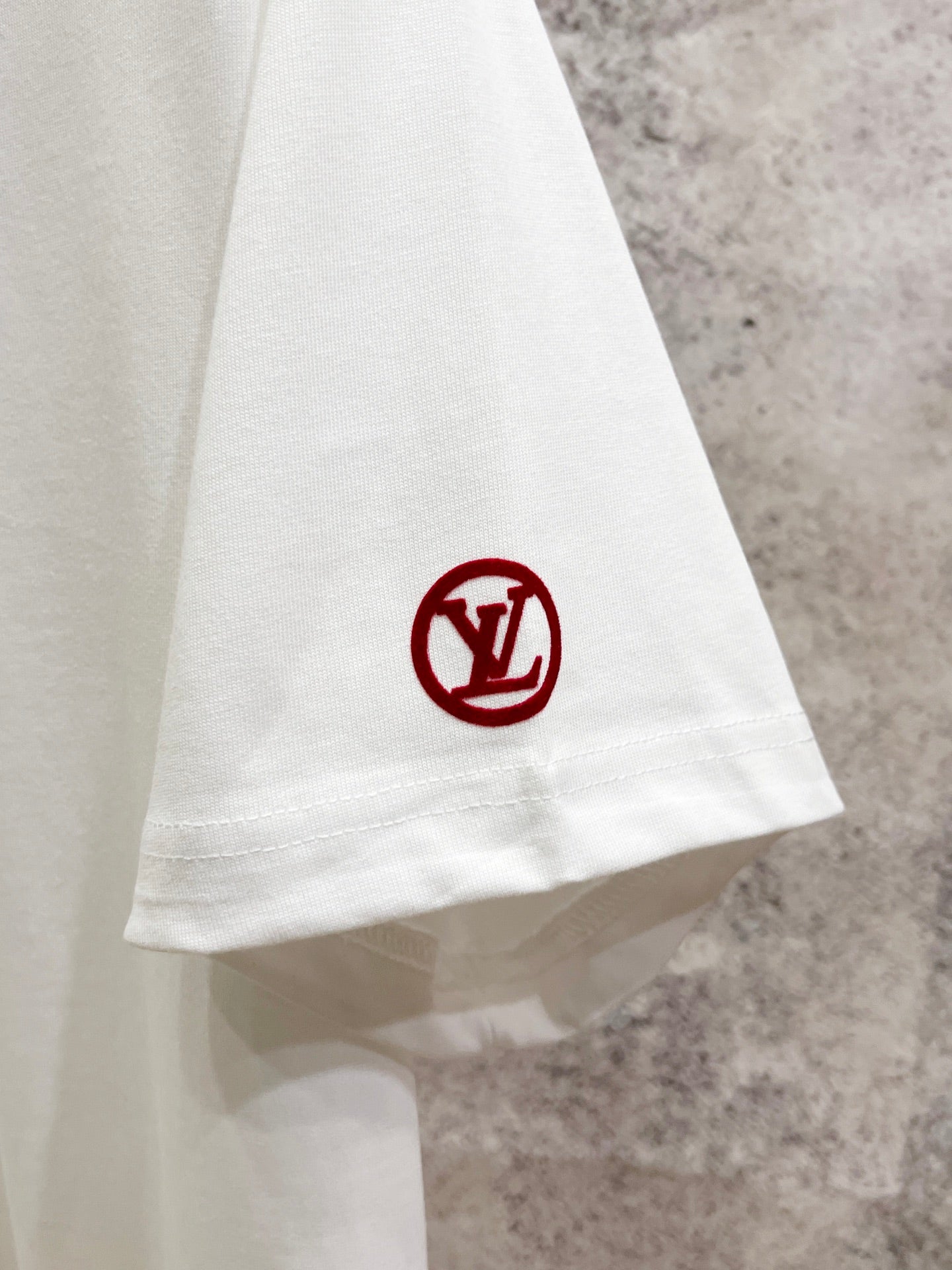 White T-shirt hem with red circular LV monogram patch.