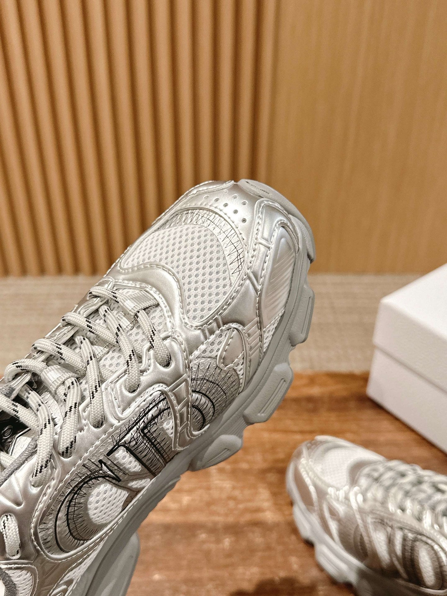 Close-up of silver metallic Dior sneaker upper with lace eyelets and stitching