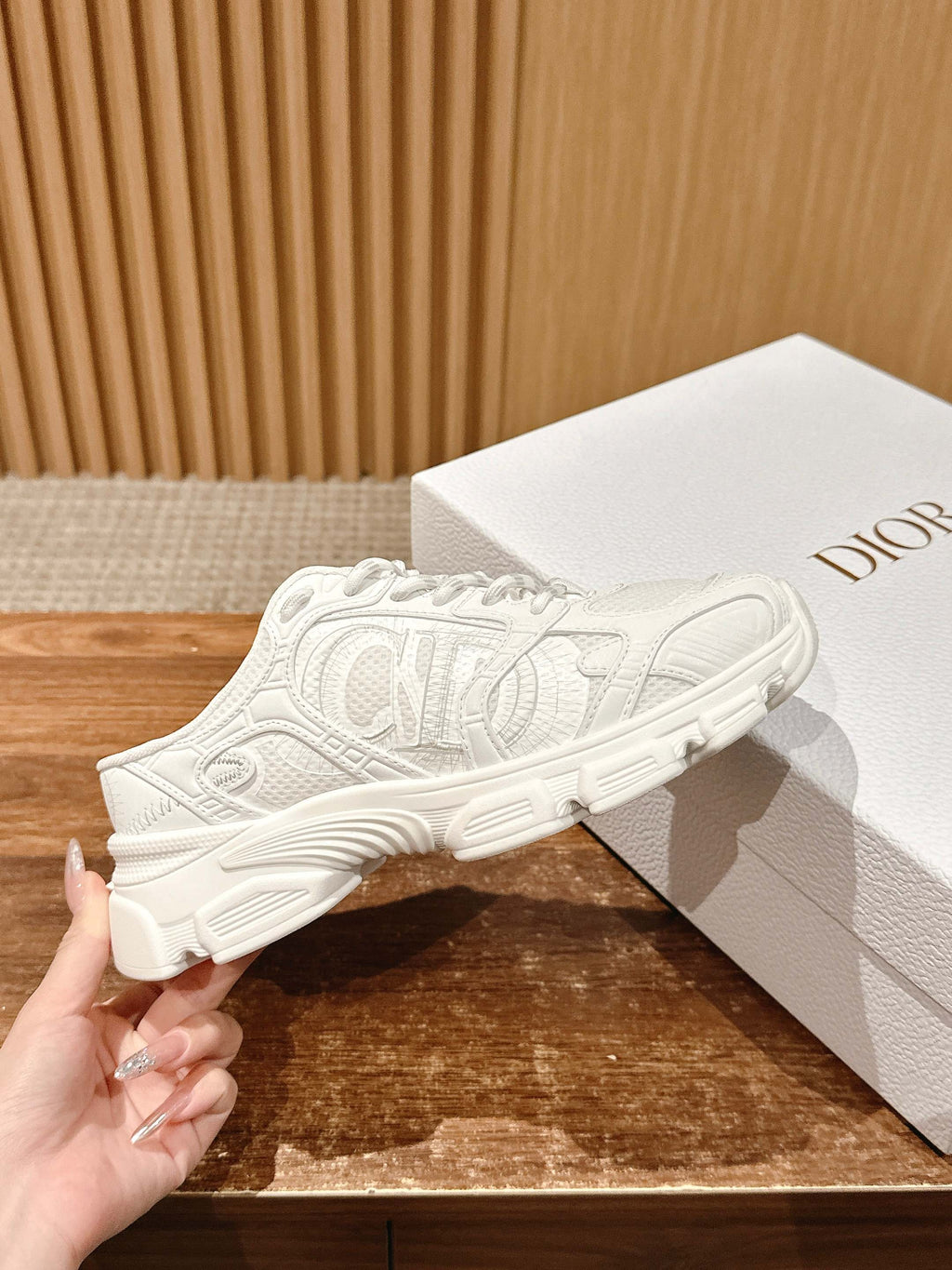 White Dior sneaker held beside a box, side profile with ridged outsole