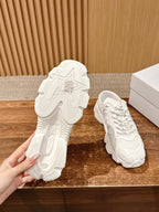 White Dior sneakers with visible outsoles, held for a bottom view