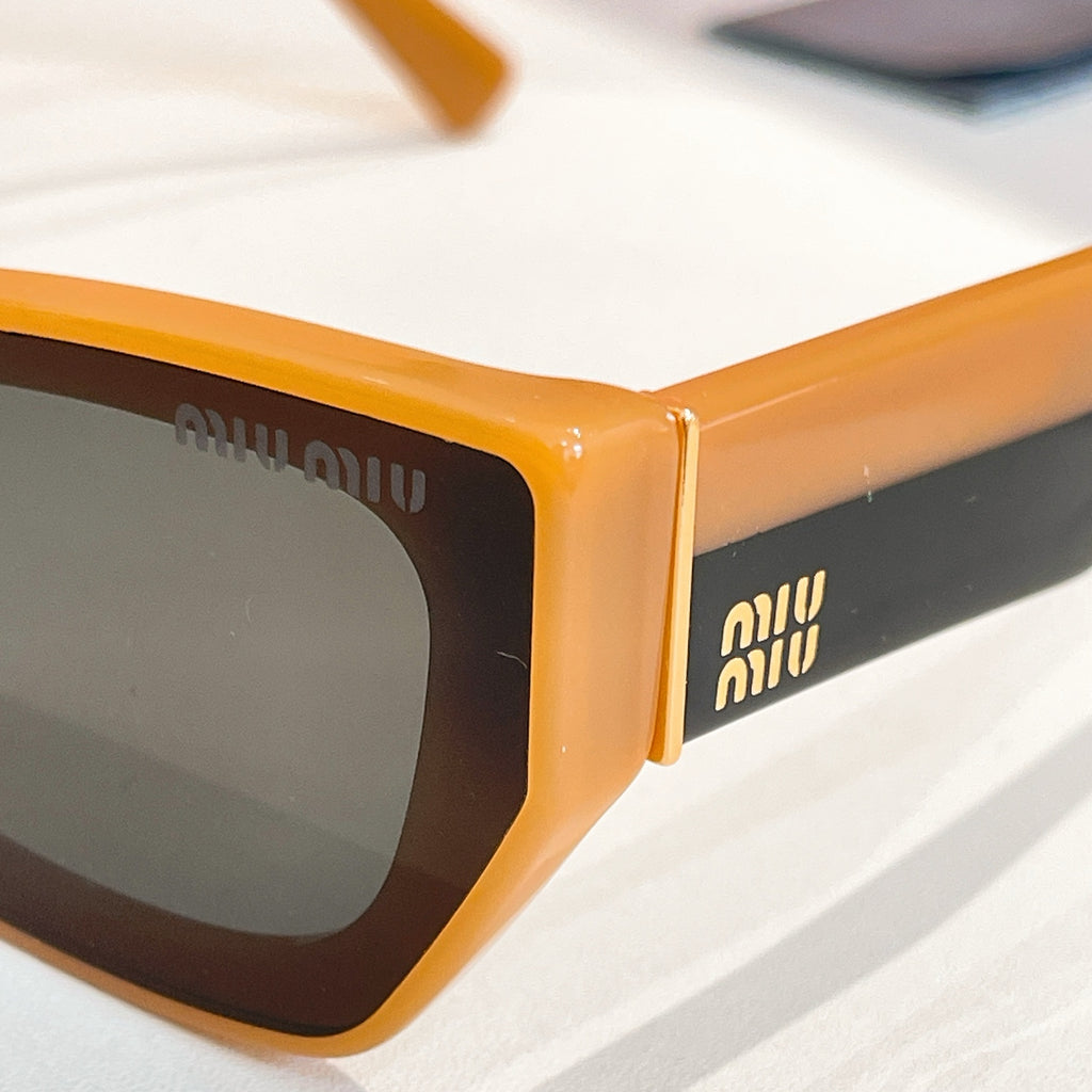MiuMiu sunglasses close-up with orange frames and dark lenses.