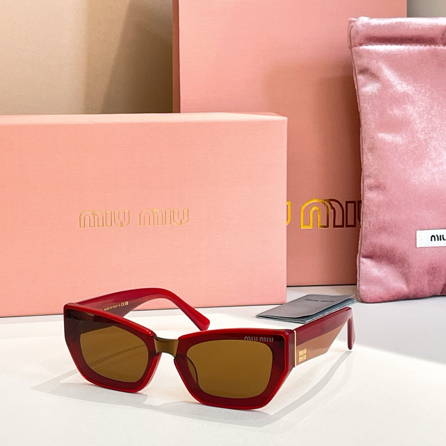 MiuMiu sunglasses with red frames and dark tinted lenses.
