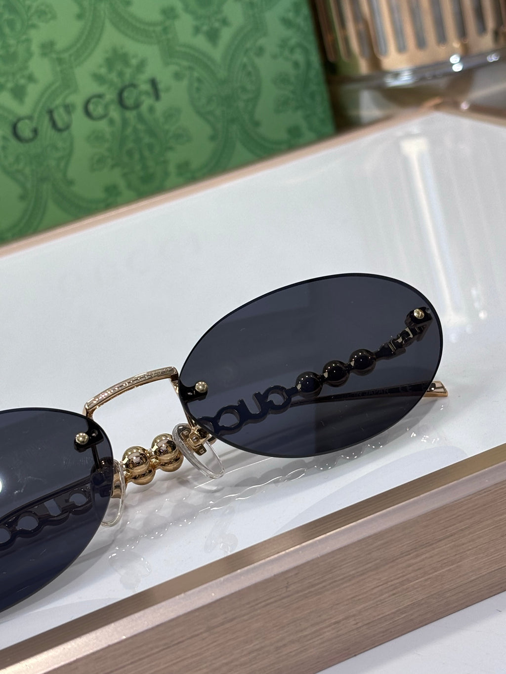 Round sunglasses close-up: dark lens, gold-tone frame, beaded chain and logo detail
