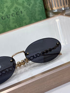 Round sunglasses close-up: dark lens, gold-tone frame, beaded chain and logo detail