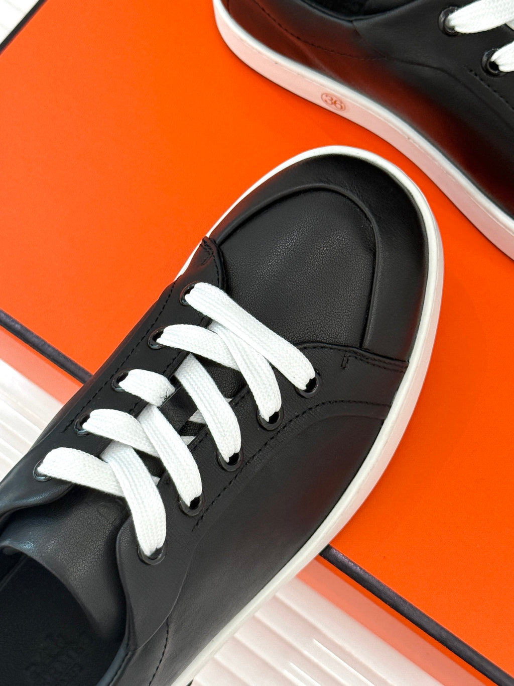 Black low-top sneaker close-up with white laces and low white rubber sole edge.