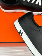 Black sneaker close-up with white sole edge and lace panel, low-top side view.