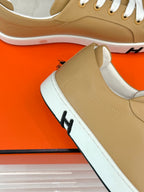 Close-up of tan Hermes sneaker side, white laces, stitched paneling and textured sole