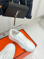 White leather sneakers on an orange shoebox, side and toe view.