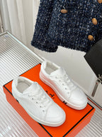 White leather lace-up sneakers on an orange shoebox.