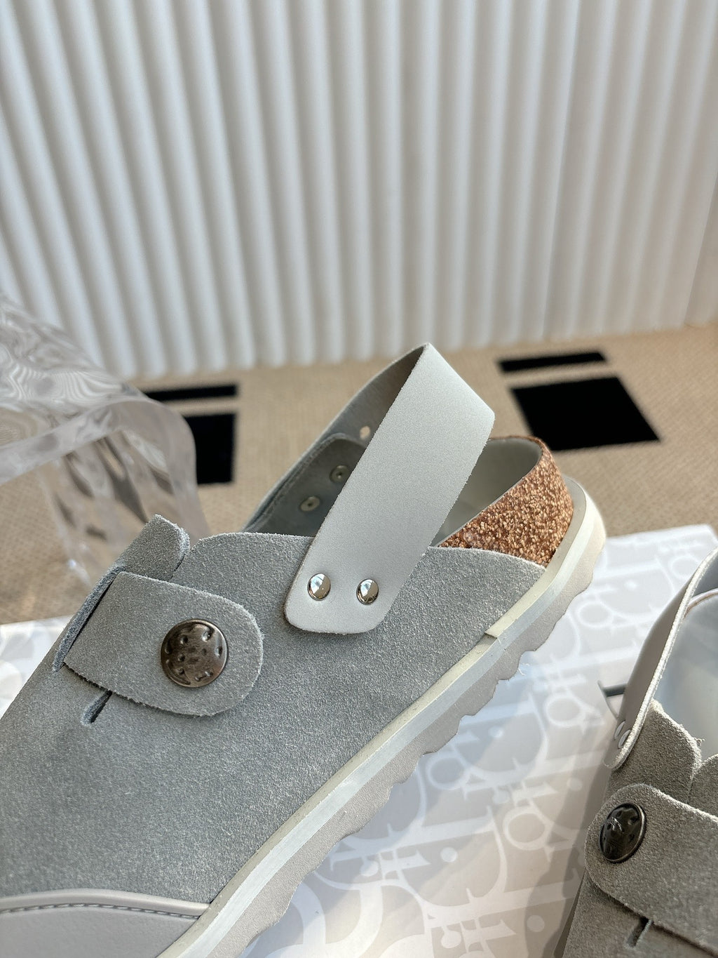 Close-up of light gray slip-on shoe with round button and strap