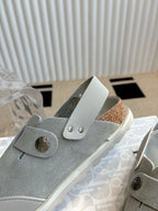 Close-up of light gray slip-on shoe with round button and strap