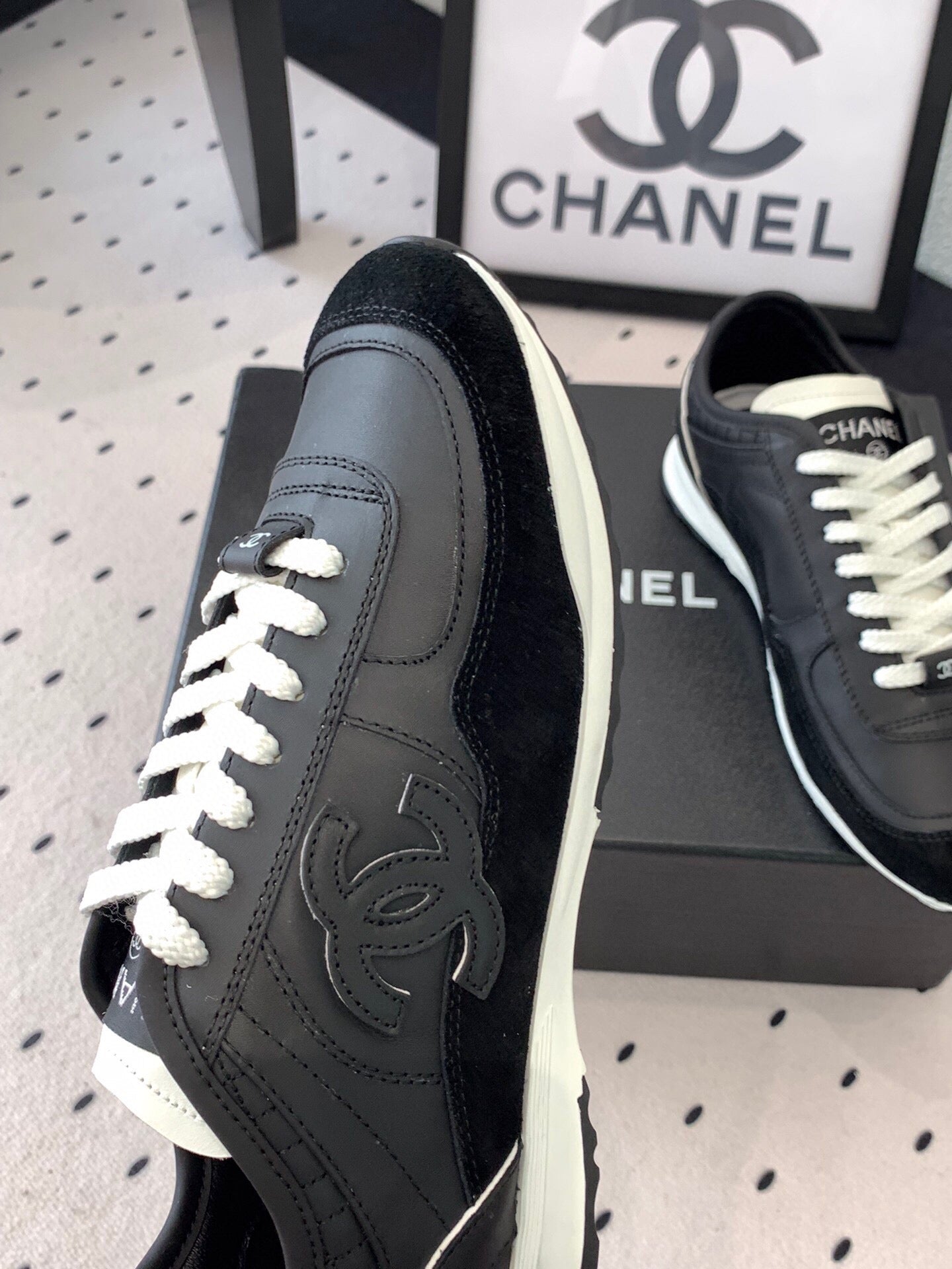 Black Chanel sneakers side view with white laces, CC logo on the quarter