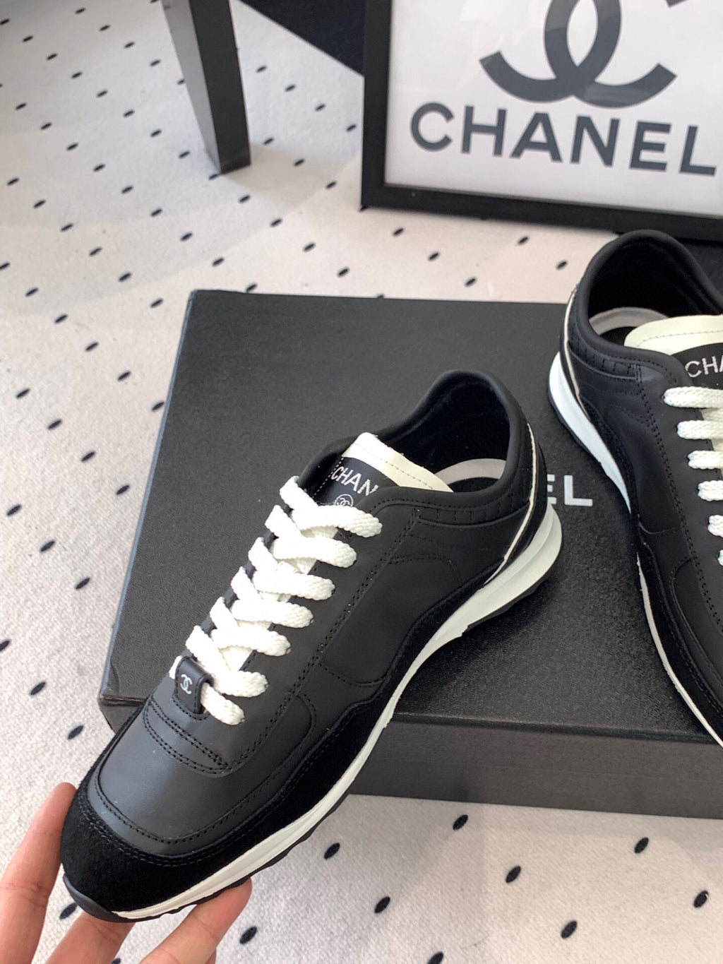 Black Chanel sneakers held up, front-left view with white laces and white sole