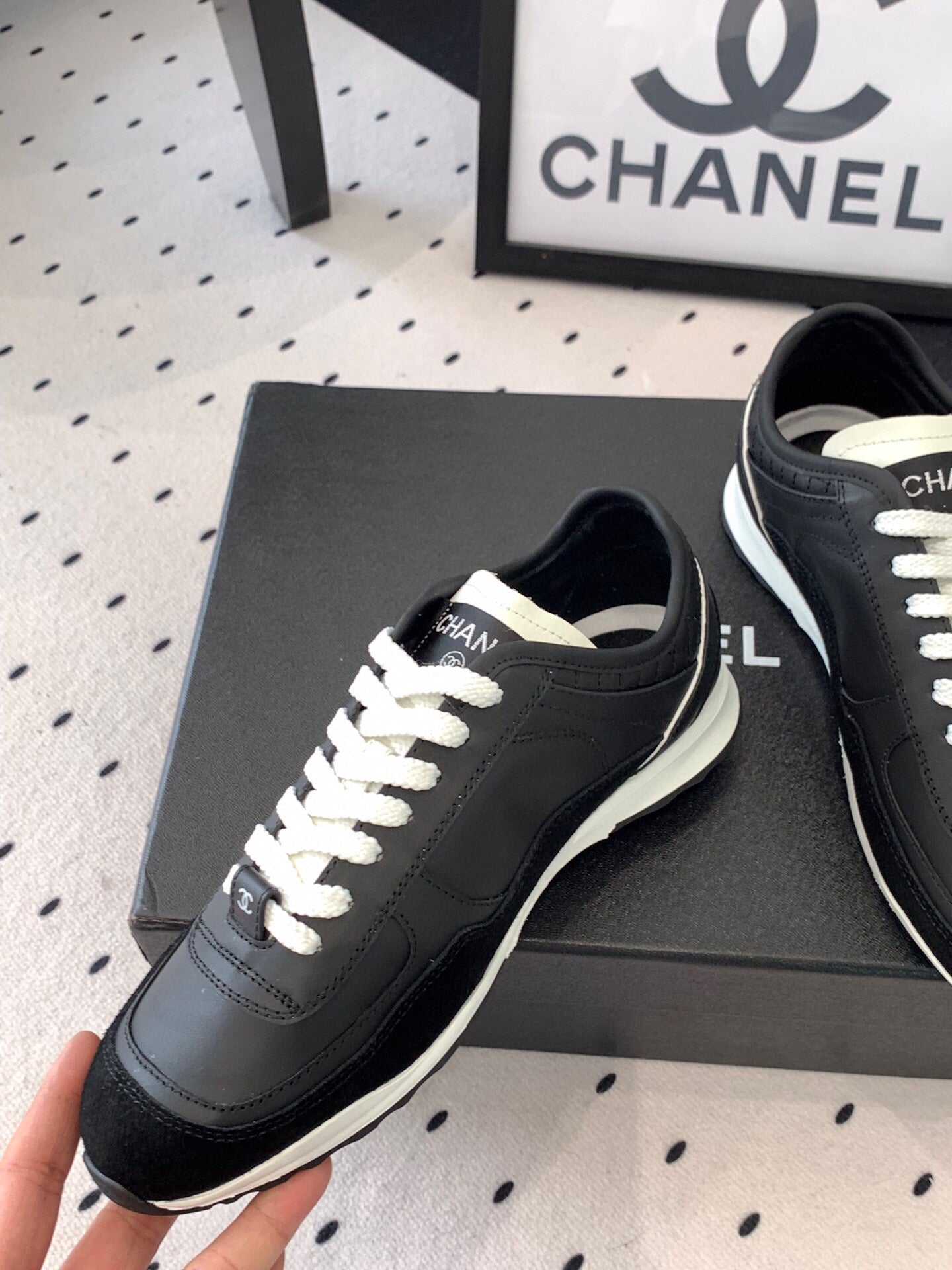 Black Chanel sneakers held up, front-left view with white laces and white sole