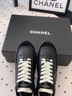 Black Chanel sneakers on a black box, white laces and CC logo on front