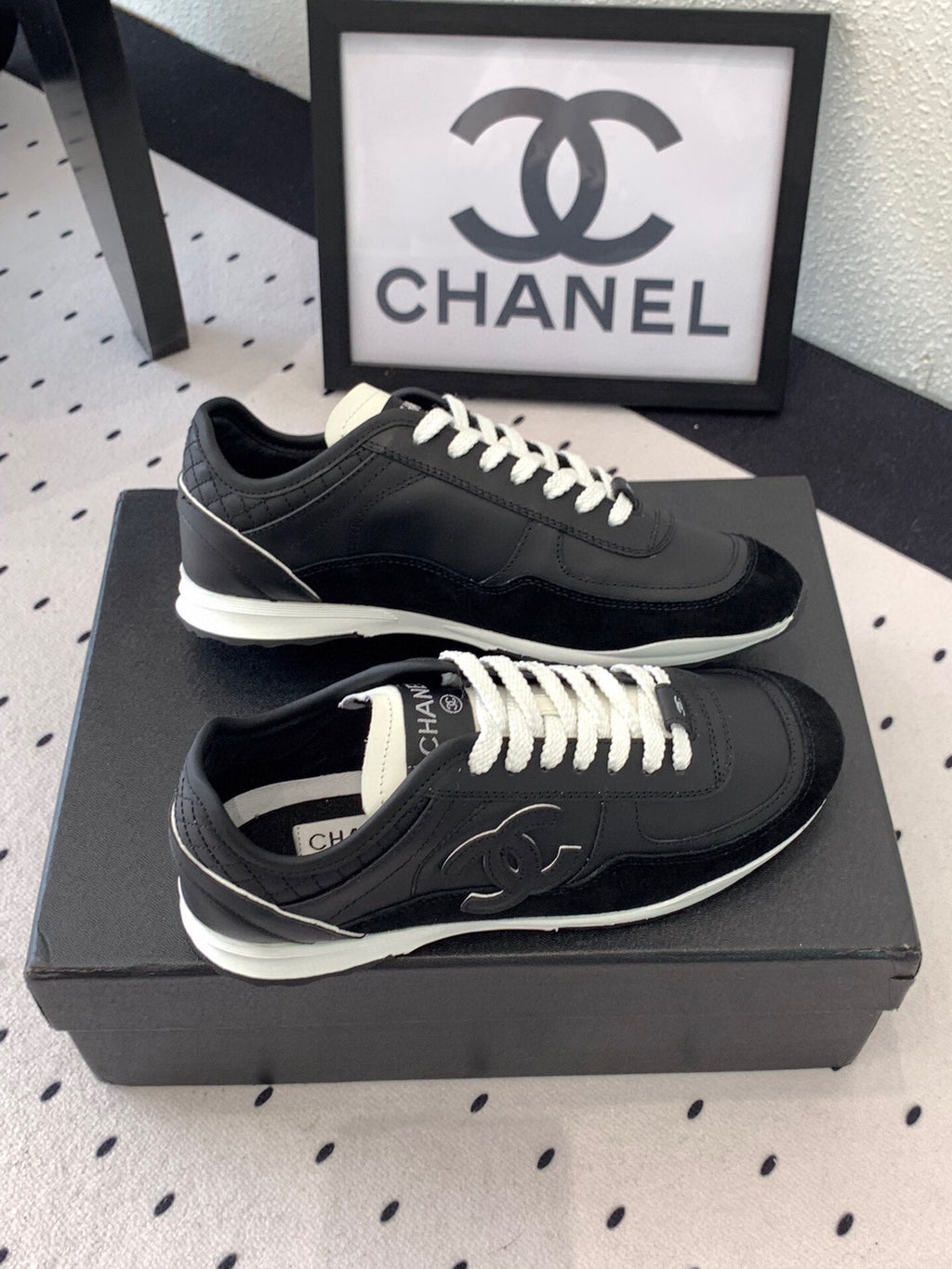 Black unisex Chanel sneakers on black box, top view with white laces