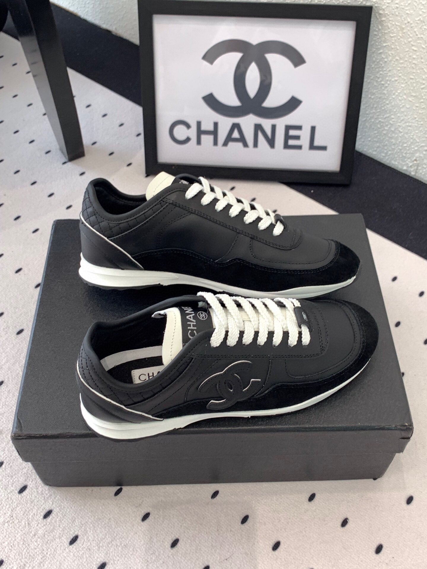 Black unisex Chanel sneakers on black box, top view with white laces