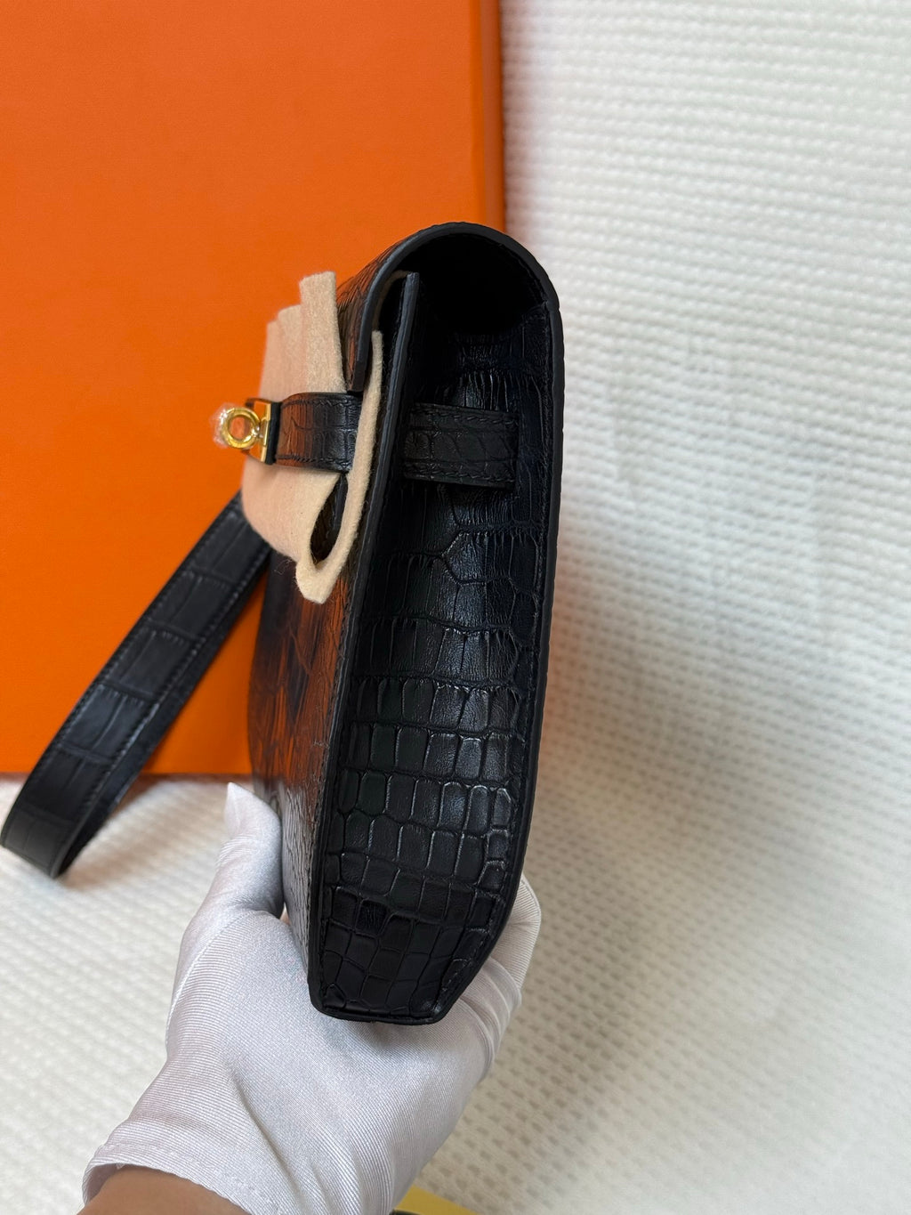 Hermes croc-embossed flap bag side view with strap and gold clasp hardware.