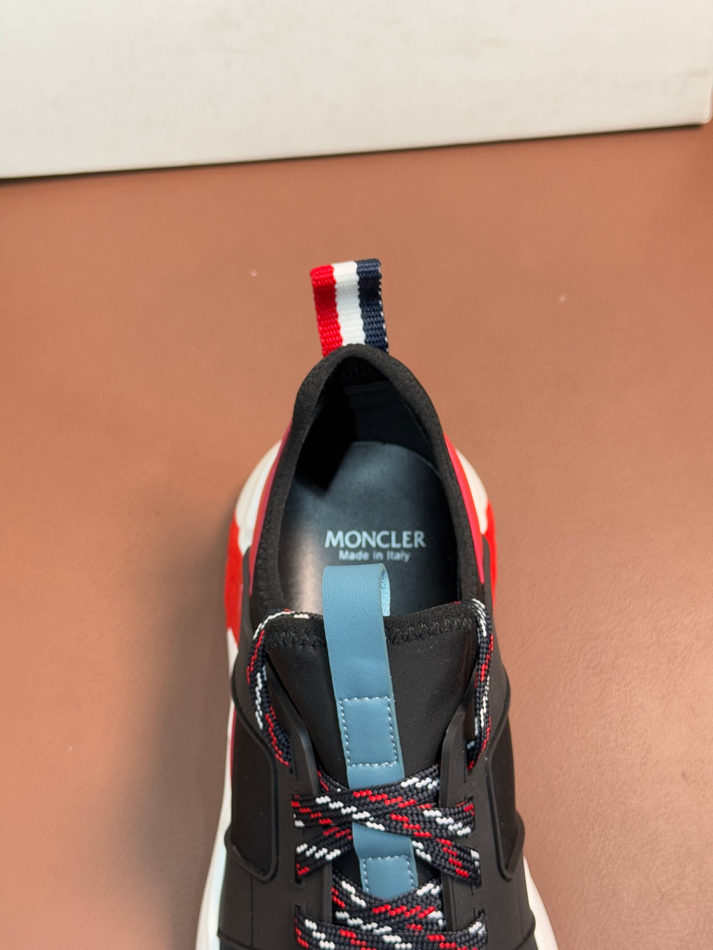 Moncler luxury shoes, black upper with red trim, light blue heel tab, and lace stitching