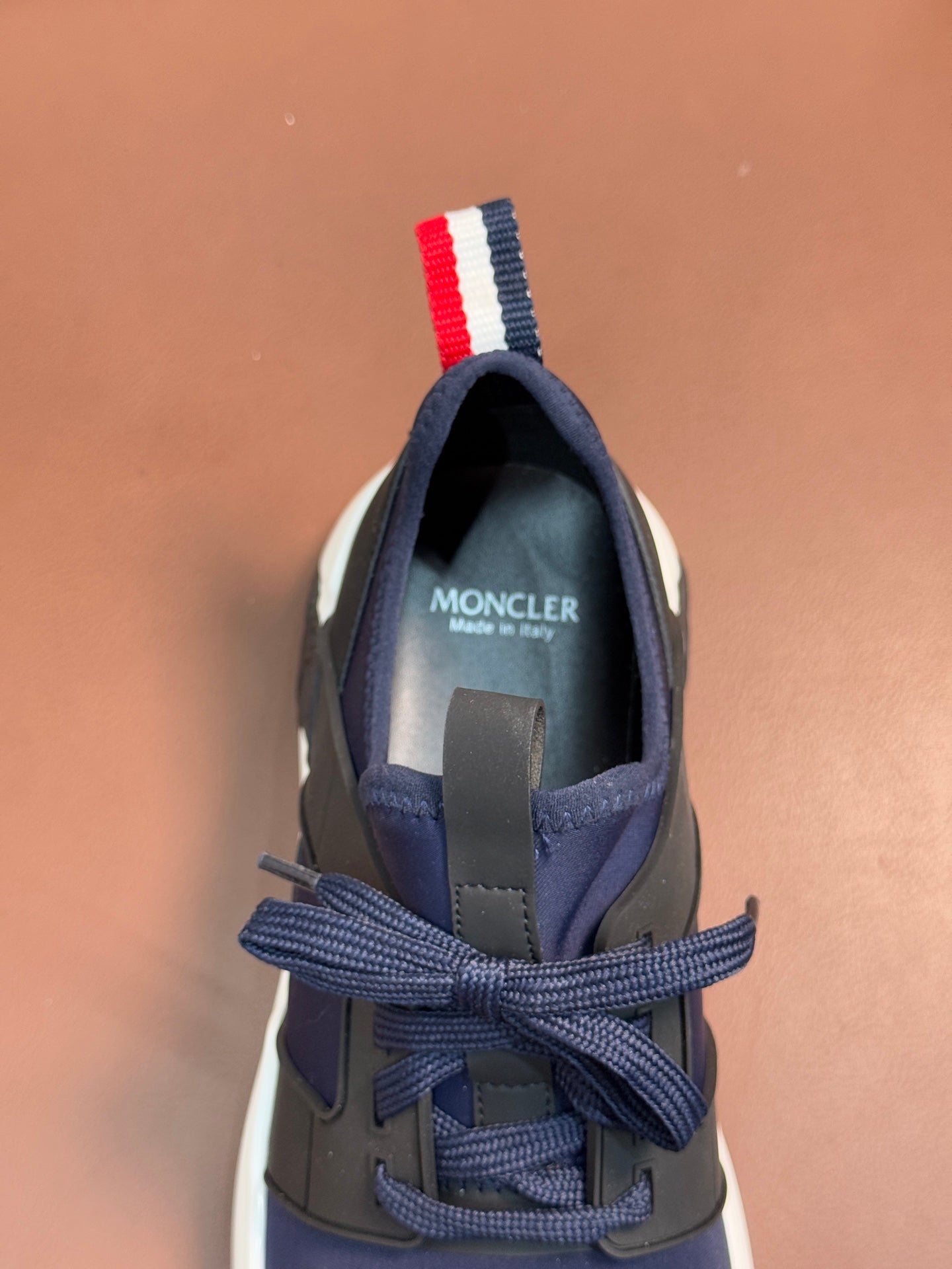 Luxury sneaker heel view with lace-up lacing, dark navy upper, and striped pull tab