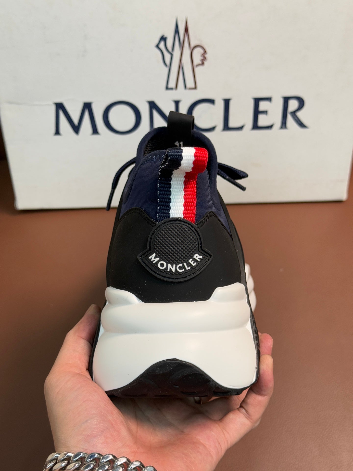 Luxury sneakers rear view held in hand, dark navy heel stripe and white midsole