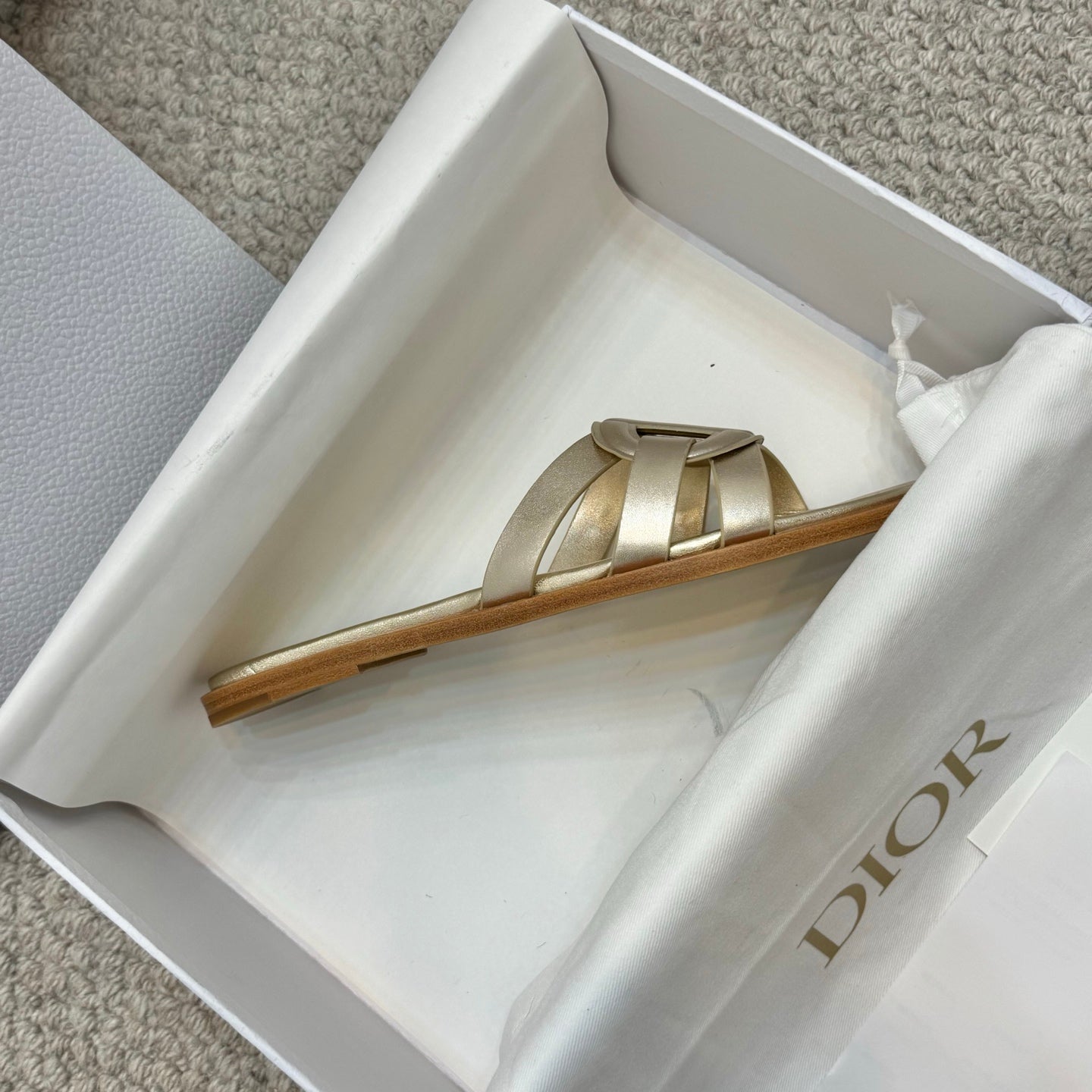 Dior gold slide sandals shown from side in box with low wooden-look sole