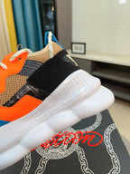 Close-up of sneaker heel and side: blue sole, black strap, orange panel, Versace details
