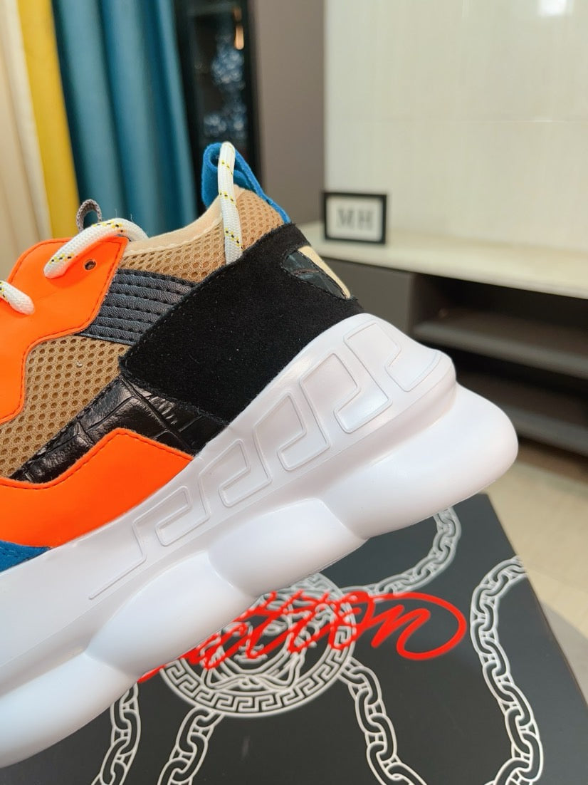Close-up of sneaker heel and side: blue sole, black strap, orange panel, Versace details